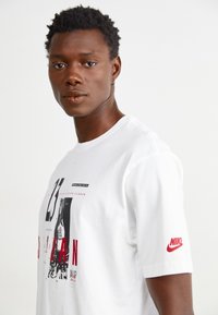 Vit bomull t-shirt med ett grafiskt tryck av en basketspelare, med röda accenter och en Nike-logotyp på ärmen. Korta ärmar.