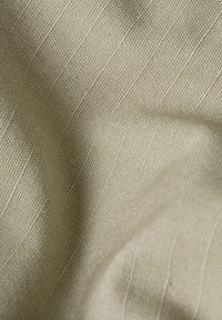 Tissu beige avec une surface texturée. Le tissage révèle un motif subtil de fines lignes et une apparence douce et lisse.