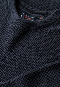 Dunkelblauer strukturierter Pullover mit geripptem Rundhalsausschnitt und subtilen, erhabenen Mustern. Markenlabel am Hals sichtbar.
