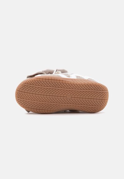 Semelle d'une basket beige et blanche montrant un motif de sculpture détaillé et des marquages de taille sur un fond clair uni.