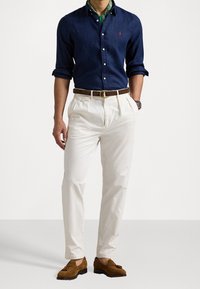 Laivansinisestä pellavapaitasta nappikauluksella on yhdistetty vaaleanbeiget pleat-housut ja ruskeat mokkasaappaat, joissa on punottu vyö.