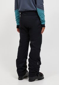 Svart vattentäta skidbyxor med vida ben, försedd med förstärkt midja och diskreta logotypdetaljer på nederbenen.