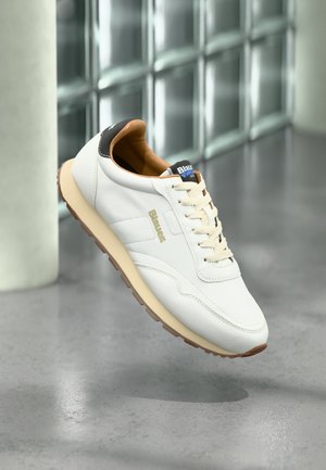 Weißer Sportschuh aus Leder mit beigefarbener Sohle, braunem Fersenakzent und beigen Schnürsenkeln. Mit dezentem seitlichen Logo und strukturiertem Obermaterial.