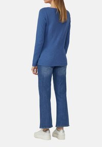 Blue long-sleeve top with a round neckline paired with light blue, straight-leg jeans and white sneakers with silver accents.