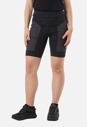 Personne portant un short de sport noir et gris foncé arrivant aux genoux avec des poches latérales zippées et des chaussures de sport noires sur un fond blanc.