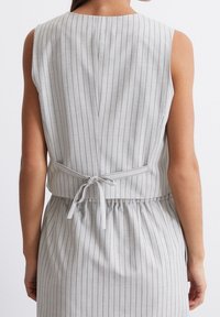 Vestido sin mangas de rayas grises con una cintura ajustada y detalle de lazo en la parte posterior. Presenta un tejido texturizado y líneas verticales sutiles.