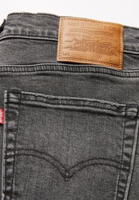 Jeans de denim gris con un parche de cuero de la marca. Presentan un diseño de bolsillo trasero curvado y una etiqueta roja en la costura del lado izquierdo.