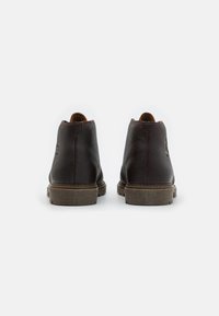 Botas de tobillo de cuero marrón con un acabado texturizado, que presentan una suela gris resistente y detalles de costura mínimos en el talón y los lados.