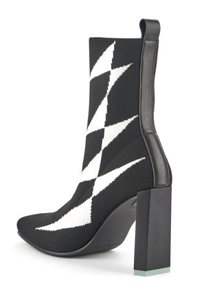 Strickstiefelette in Schwarz mit weißem Zickzackmuster, spitzer Zehenform und Blockabsatz, der an der Basis einen transparenten Akzent aufweist.
