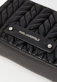 Borsa a tracolla nera in pelle trapuntata con un pannello inferiore liscio, hardware metallizzato e una tracolla firmata con testo incastonato.