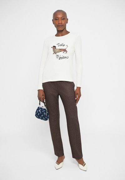 Langsleeve crèmekleurig shirt met een teckelafbeelding, bruine gebloemde broek en witte schoenen. Donkerblauwe tas met patroon, slim fit.