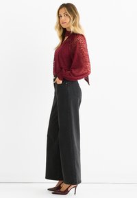 Burgundy sheer blouse with a keyhole neckline and long, elasticated sleeves paired with high-waisted black wide-leg jeans and pointed heels.
