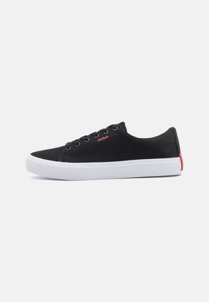 Black canvas sneakers with a white rubber sole, featuring a red accent at the heel and black laces. "HUGO" logo in red on the side.