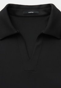 Chemise noire à col avec un col en V et une étiquette au niveau de l'encolure indiquant « someday ».