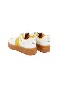 Sneakers bianchi con dettagli gialli, suola in gomma testurizzata, punta rotonda e logo sul tallone. Presentano un colletto imbottito e un sistema di allacciatura.
