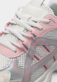 Λευκό και ροζ αθλητικό παπούτσι με ύφασμα από δίχτυ, αντανακλαστικές γκρι λεπτομέρειες και λευκά κορδόνια δεμένα πάνω σε ροζ πάνελ με τρύπες.