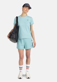 Světle modré sportovní tričko a šortky z bavlny, doplněné černou taškou. Bílé tenisky s barevnými pruhovanými ponožkami.