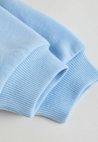 Tissu de pull bleu clair avec des poignets côtelés, montrant une texture douce et une finition lisse, plié soigneusement pour révéler les détails et la couleur.
