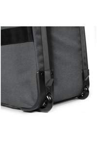 Valigia rotolante in tessuto grigio scuro con accessori neri. Presenta un'esterno testurizzato, angoli rinforzati e ruote fluide multidirezionali.