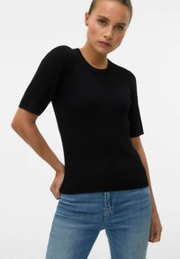 Svart ribbad kortärmad tröja med rundad hals; figurnära design som framhäver den strukturerade tyget. Kombinerad med ljusblå jeans.