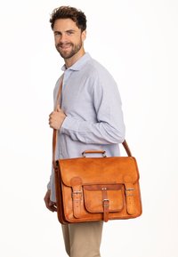 Borsa a tracolla in pelle marrone con pattina, tasca frontale e chiusura a doppia fibbia. Presenta una maniglia superiore e una tracolla regolabile.