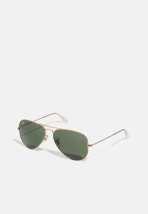 Occhiali da sole aviator con lenti verdi, montatura in metallo dorato, naselli trasparenti e stanghette sottili. Design minimalista con una forma classica.