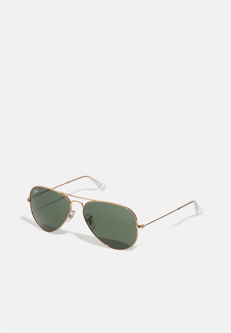 Ochelari de soare aviator cu lentile verzi, ramă din metal auriu, tampoane nazale transparente și tempuri subțiri. Design minimalist cu o formă clasică.