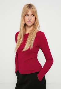 Top rosso a maniche lunghe con costine, silhouette aderente, scollo rotondo e cuciture piatte, abbinato a pantaloni neri. Tessuto liscio e design sobrio.