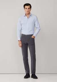 Camisa de botones a rayas azul claro, pantalones grises y zapatos oscuros; textura suave, corte entallado, con un cuello clásico y bolsillos frontales.