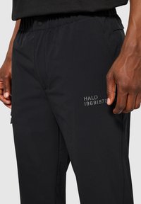 Schwarze Stretchhosen mit einem elastischen Bund, die auf der Seite eine dezente Stickerei "HALO 1968-1978" und eine glatte Textur aufweisen.