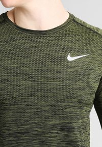 Mörkgrön träningströja med ett texturerat mönster, med rund halsringning och en vit Nike-logotyp på vänster bröstområde.