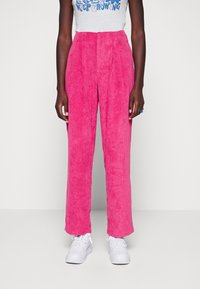 Pantalones de pana fucsia con costillas verticales, cintura alta y piernas anchas, combinados con zapatillas blancas. Textura suave y un ajuste entallado.