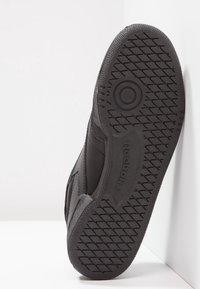 Chaussure de sport noire avec une semelle en caoutchouc texturée, une tige en cuir lisse et des lignes de design subtiles. Présente le logo Reebok sur la semelle.