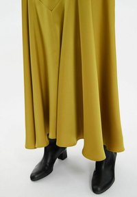 Jupe longue et fluide de couleur jaune avec une texture douce et un décolleté en V, associée à des bottines noires à bout pointu avec un talon épais.