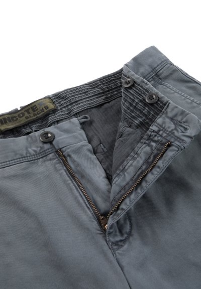 Pantaloni grigi con cerniera parzialmente aperta, vita con bottone e etichetta interna in tessuto visibile con la scritta "PINGOTEX SLACKS."