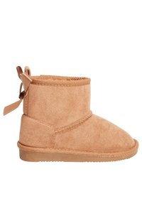 Stivaletti alla caviglia in suede beige con punta arrotondata, texture morbida, dettagli cuciti e un fiocchetto decorativo sul retro. Suola piatta in gomma.