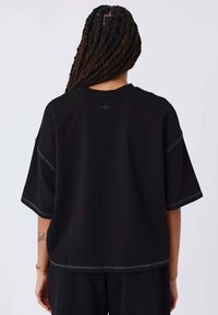 T-shirt nera oversize in cotone, con spalle scese, cuciture a contrasto e un dettaglio a forma di stella vicino al collo.