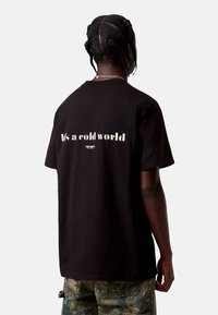 Czarna bawełniana koszulka z krótkimi rękawami. Z tyłu znajduje się biały tekst "To zimny świat" oraz małe logo. Tekst jest pogrubiony i lekko zniszczony.