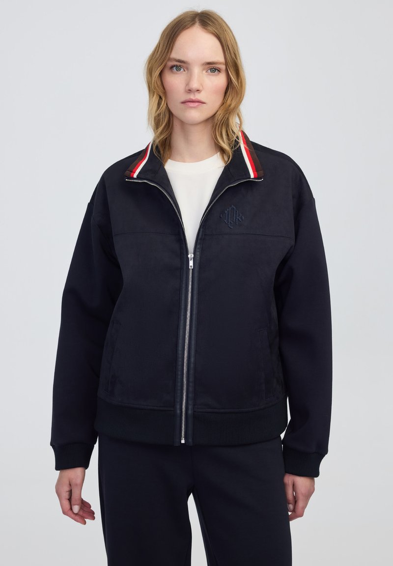 Chaqueta de navy con cremallera y cuello a rayas rojas y blancas. Tejido suave, corte relajado, logo bordado en el pecho, puños acanalados y dobladillo.