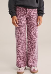 Pantalone širokog kroja s ružičastim leopard uzorkom, meke teksture, s detaljnim šavovima, u kombinaciji s svijetloružičastim cipelama s bijelim vezicama.