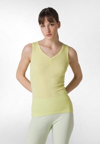 Lichtgele mouwloze top met een V-hals en geplooid detail in het midden; gladde stof; gecombineerd met lichtgroene leggings.