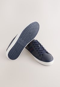 Mørkeblå syntetiske sneakers med stribede detaljer, gummisål med sekskantet mønster og snørelukning. Hvid detaljeret mellemsål.