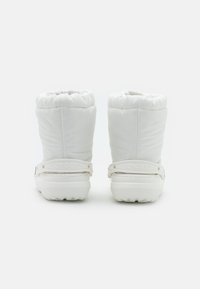 Botas brancas à prova d'água com uma parte superior acolchoada, colarinho elástico e uma sola em borracha sólida com um logótipo na alça traseira.