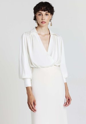 White, long-sleeve blouse with a deep V-neck and loose fit, featuring a silky texture and subtle pleats on the shoulders.