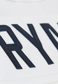 Nahaufnahme von schwarzen gestickten Buchstaben "R" und "Y" auf weißem Stoff, die detaillierte Stickerei und Stoffstruktur zeigen.