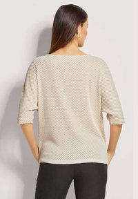 Licht beige, gebreide trui met een losse pasvorm, driekwartmouwen en een gestructureerd patroon. Heeft een ruime halslijn en een ribbelrand.