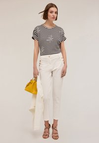 Striped t-shirt with rolled sleeves, white tailored pants with gold buttons, yellow handbag, and strappy beige sandals.