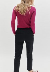 Maglione fucsia realizzato in un morbido tessuto a maglia, abbinato a pantaloni neri su misura con tasche posteriori e vestibilità slim.