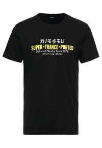 Musta puuvillapaita, jossa on rohkeaa keltaista ja valkoista tekstiä, mukaan lukien japanilaisia merkkejä ja lause "SUPER+TRANCE+PORTED." Lyhyet hihansuut.