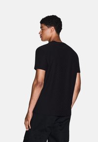 T-shirt nero a maniche corte con un motivo geometrico testurizzato e scollatura rotonda, realizzato in un tessuto leggero. Dettagli di cuciture visibili.
